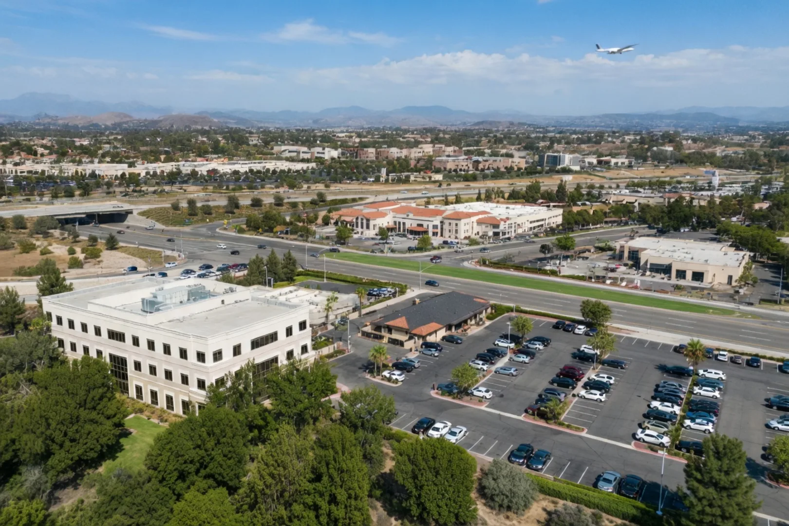 Aerial view of Murrieta's commercial corridor near Interstate 15 with mid-rise office buildings, retail centers, and a small plane in the distant sky